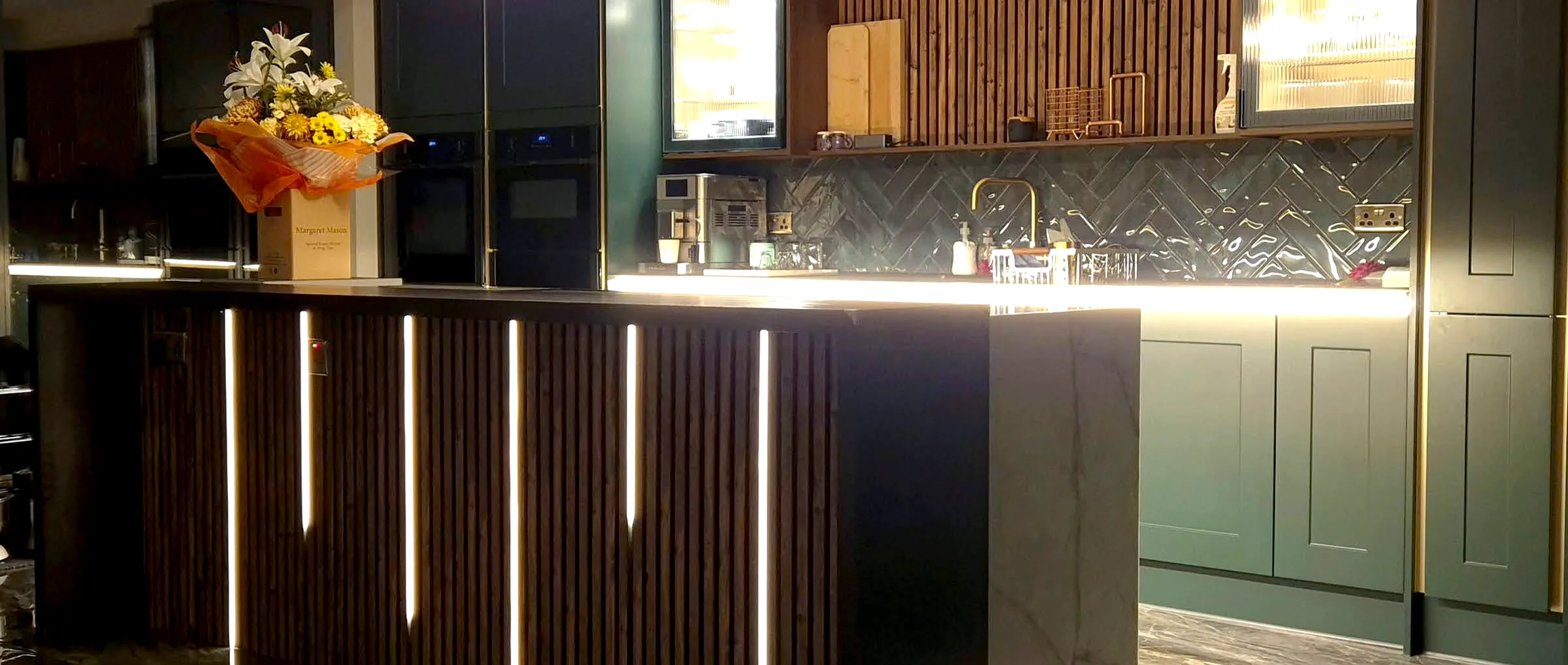 A green shaker kitchen with a walnut-slatted island lit from beneath, fitted by DC Carpentry & Construction