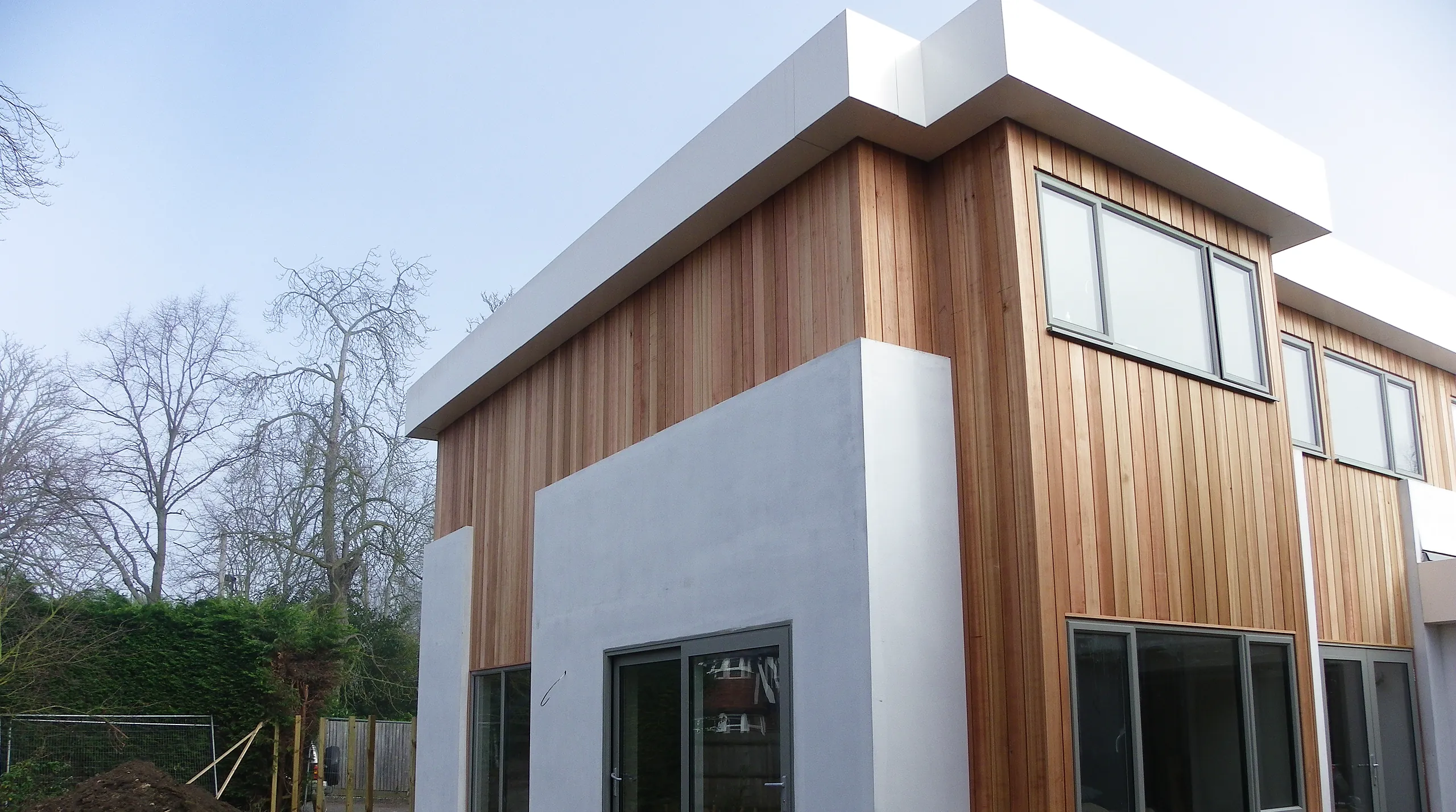 A two-storey extension finished in white render and cedar cladding