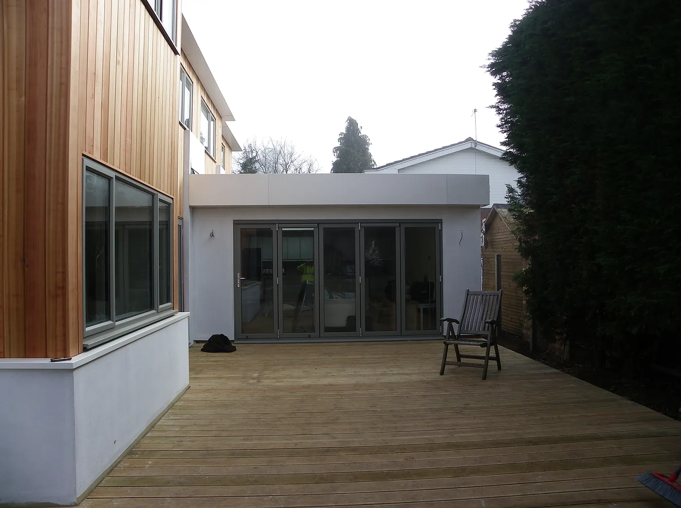 The finished rear, cedar cladding over white render with bifold doors onto a new deck