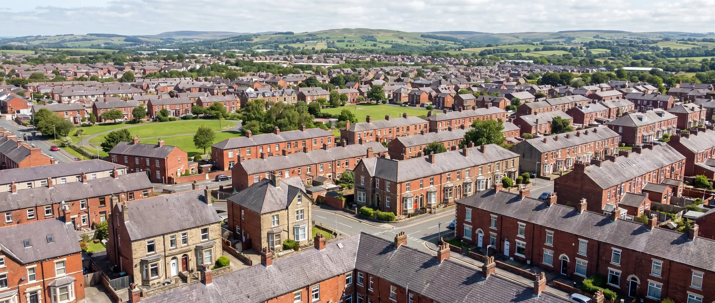 A wide view over a Lancashire town of red brick terraced and semi-detached houses with green hills behind